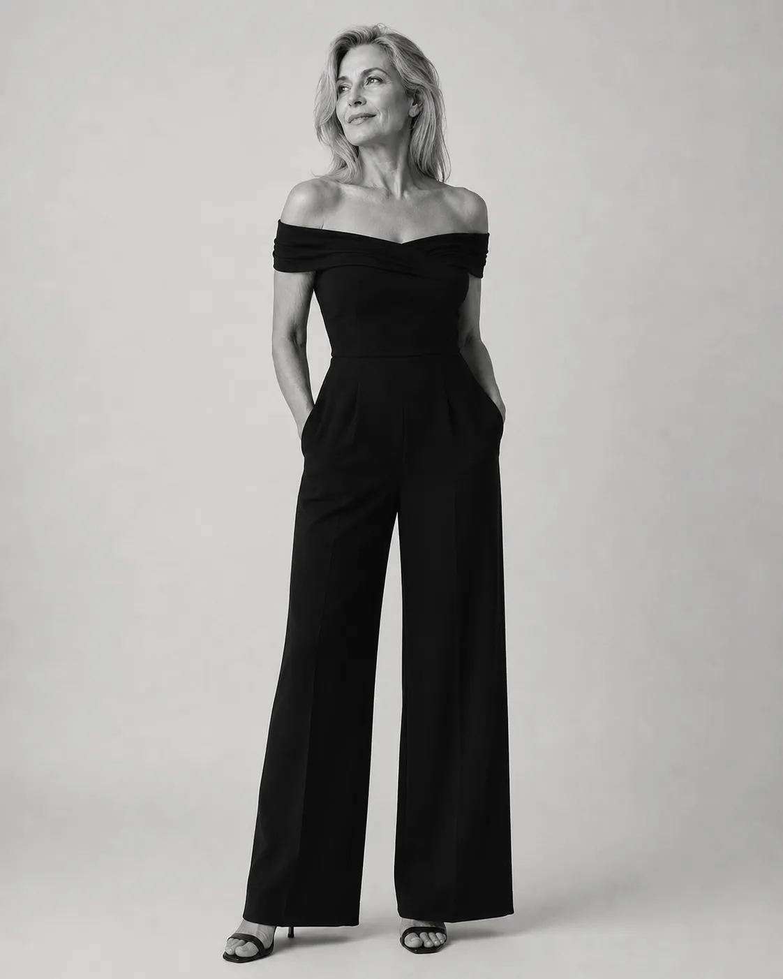Black and white studio portrait of a woman in a black off-shoulder jumpsuit