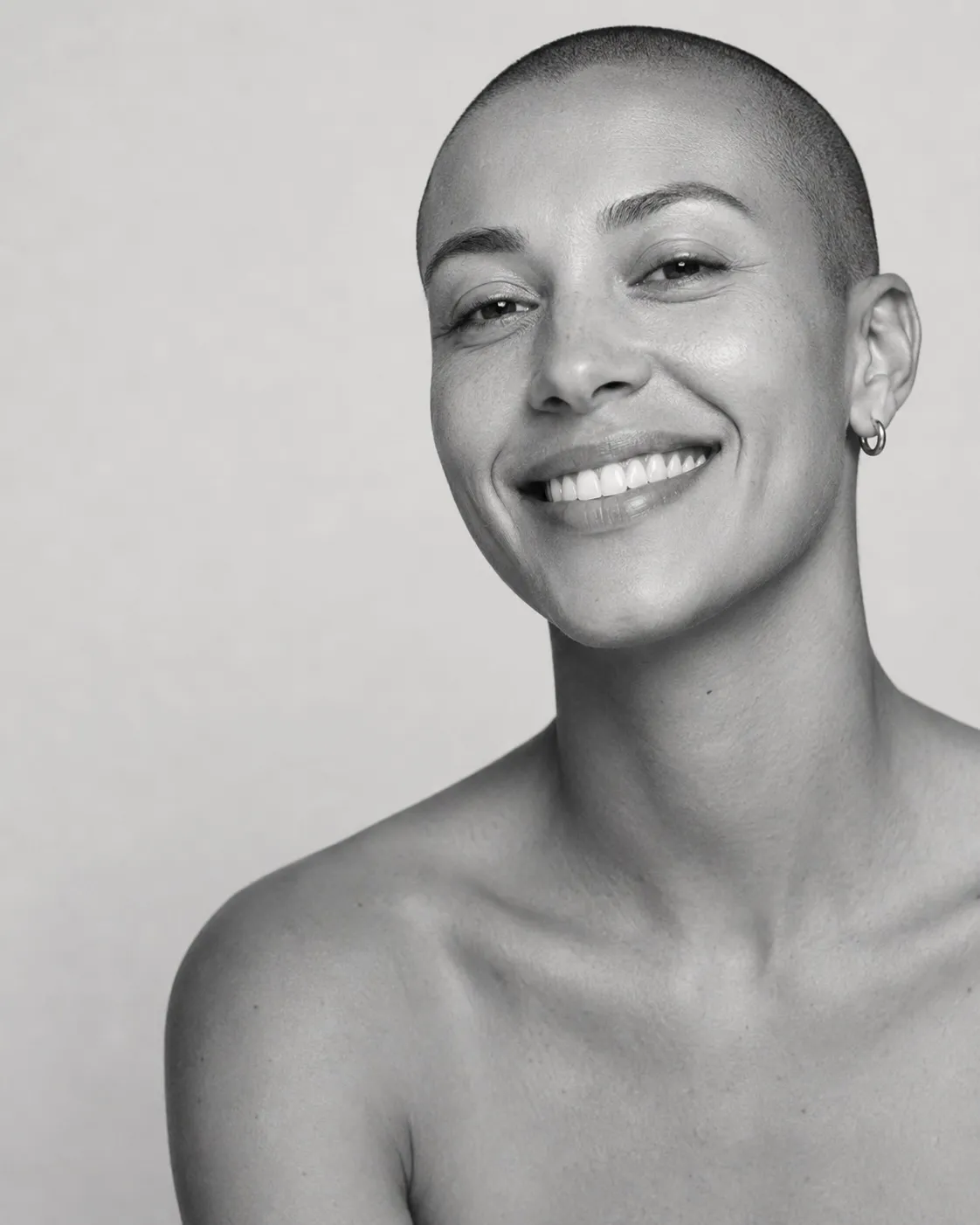 Black and white studio portrait of a smiling person with a closely shaved head